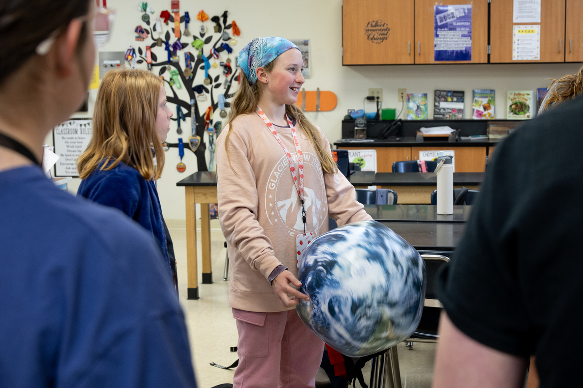 A girl smiles holding a planet earth beach ball in a science classroom. 