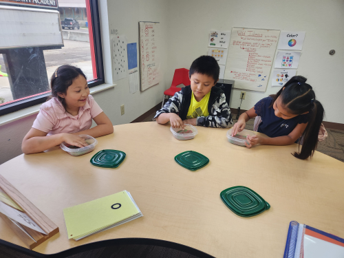 Students from Kwiyagat Community Academy write sounds they hear in the sand during a reading session with tutor Jessica Magie. 