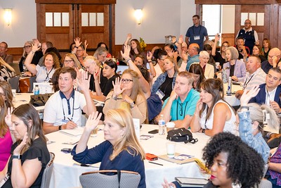 Dozens of educators seated at a conference, raising hands and listening