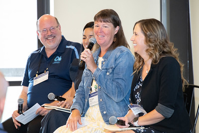 Educators with microphones presenting at a conference, smiling and laughing