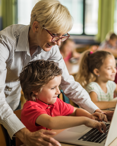 Teacher helping a young child work on a computer in a classroom setting