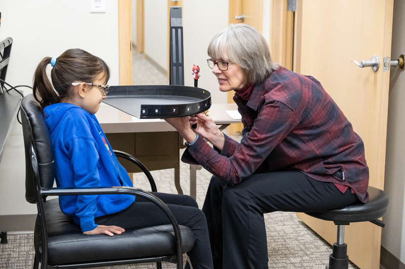 A woman holds up a black half circle and small tiger in front a girl to test peripheral vision.