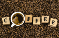 The word coffee with each letter on a wooden block except for the o which is a coffee cup. Background of coffee beans.